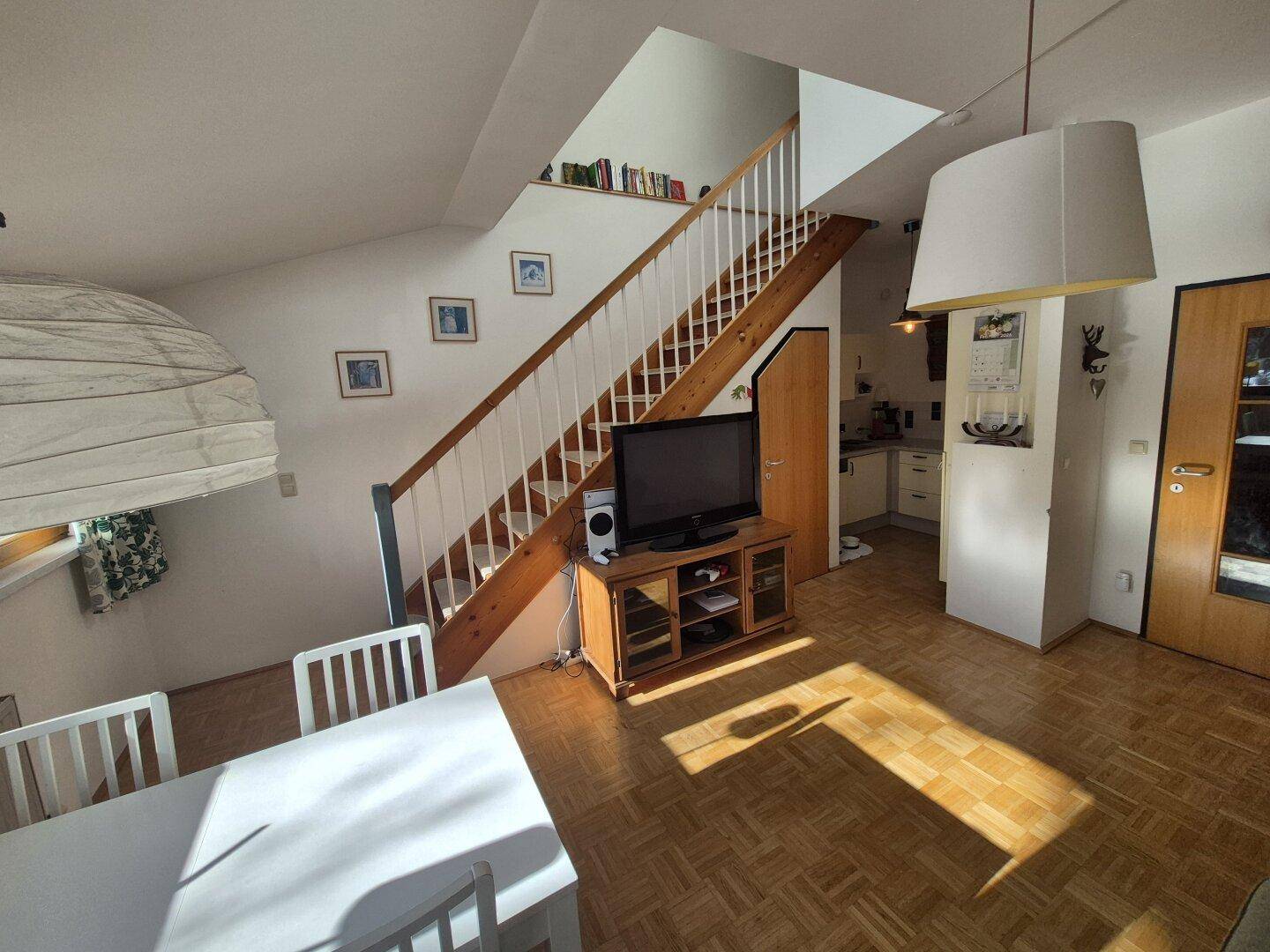 Lichtdurchfluteter Wohnbereich mit Holzboden, Esstisch und offenem Treppenaufgang.