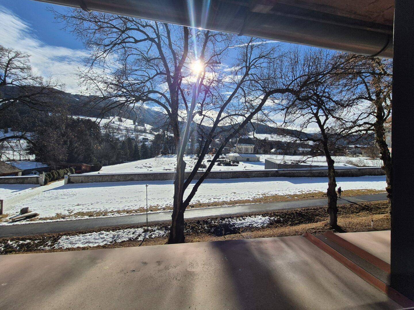 Winterliche Aussicht auf verschneite Felder und Berge von einem Fenster aus.