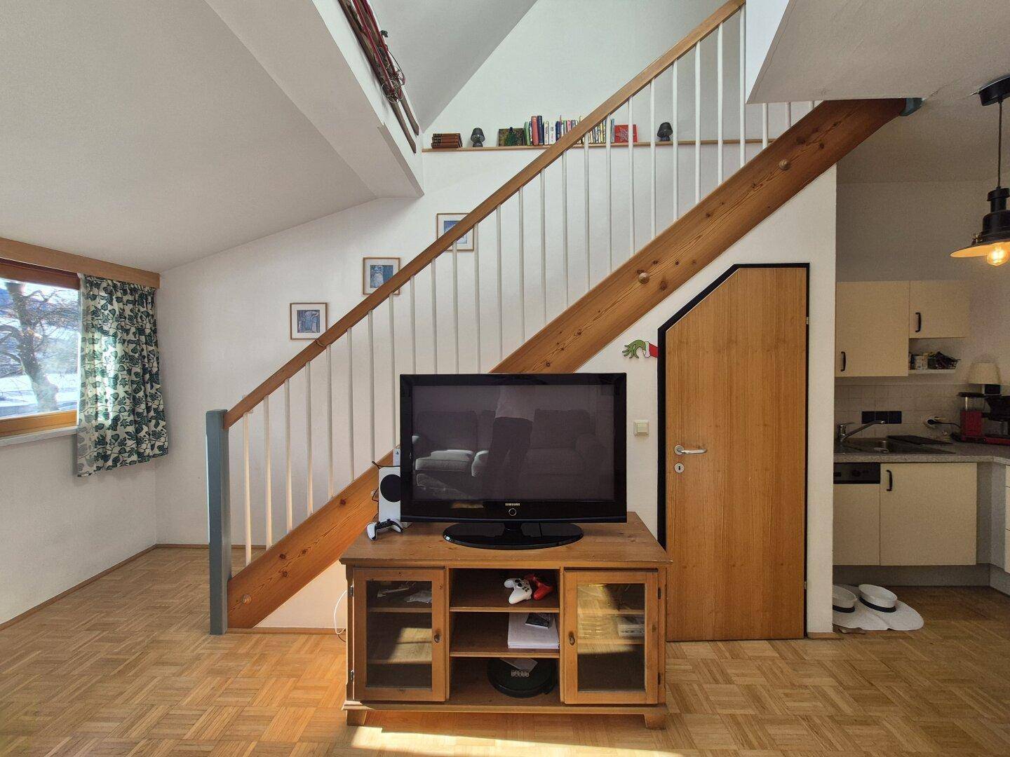 Wohnbereich mit TV-Möbel, Holzboden und offenem Übergang zur Küche.