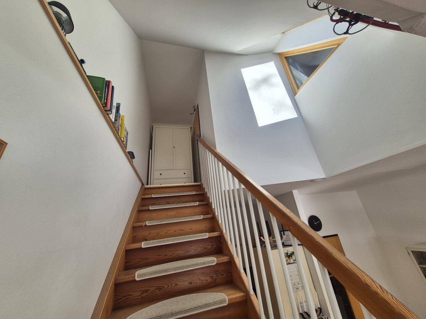Helle Holztreppe mit Teppichstufen und Oberlicht, die zu den oberen Etagen führt.