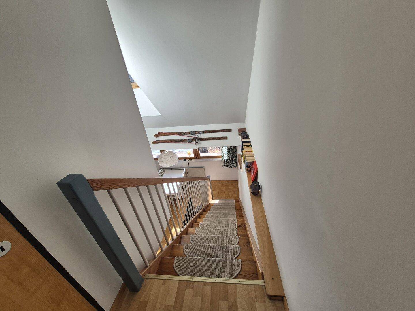 Holztreppe mit Teppichstufen und Blick nach unten in den Wohnbereich.