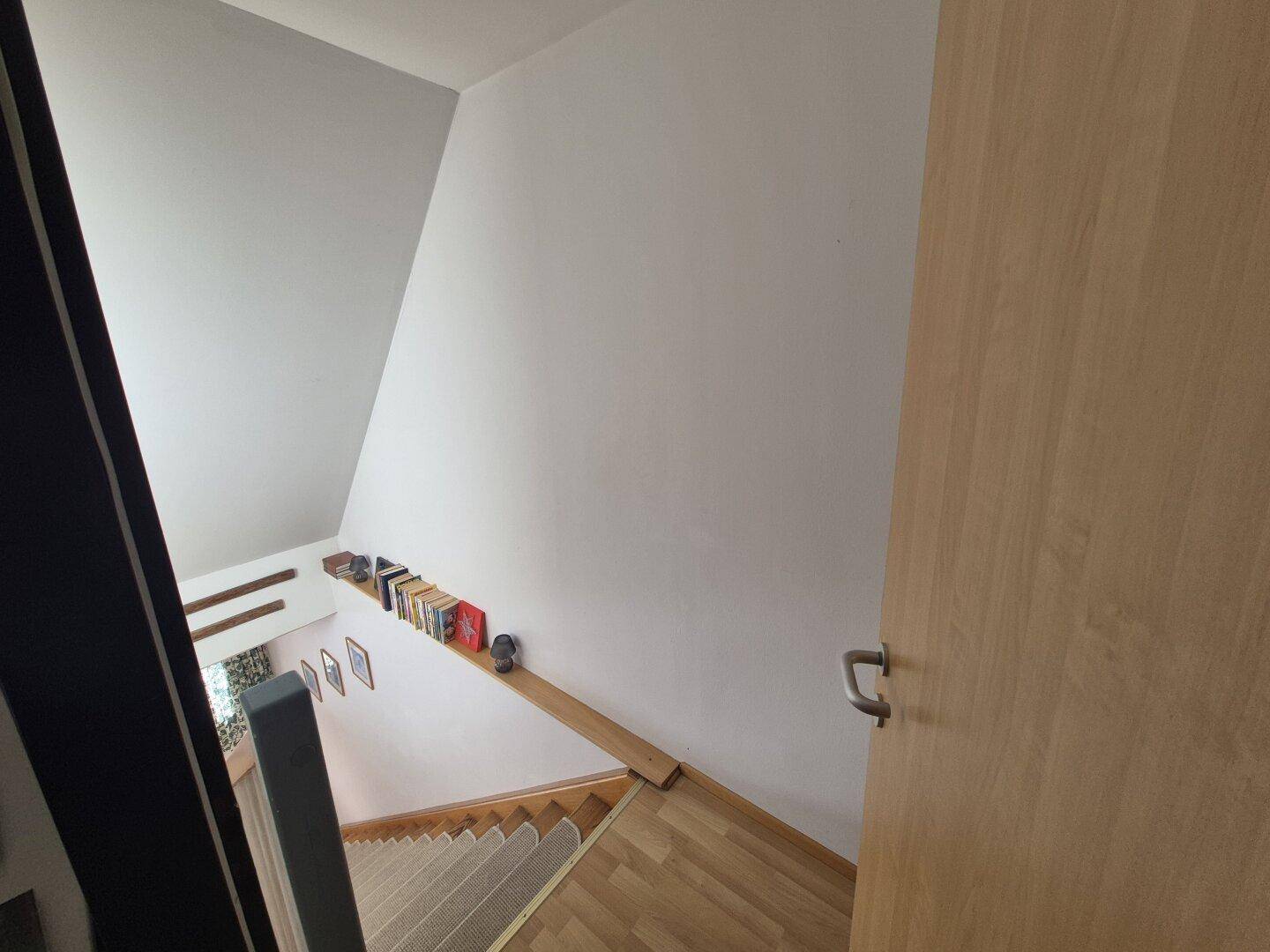 Treppenaufgang mit Holzboden und weißer Wand, der zu den oberen Etagen führt.