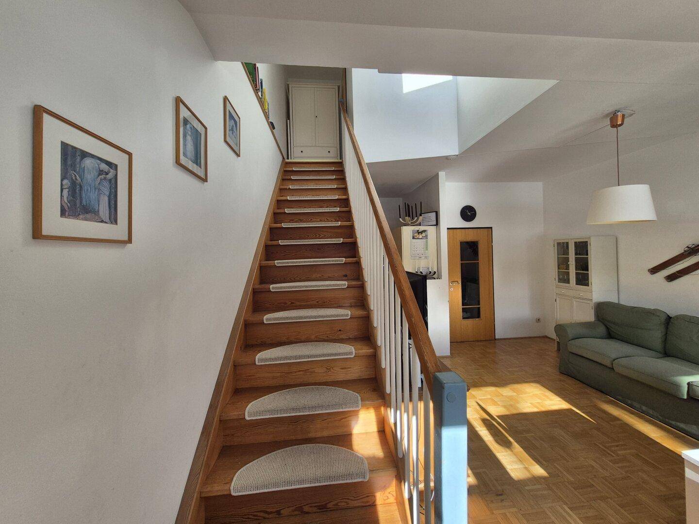 Holztreppe mit weißem Geländer und Blick in den offenen Wohnbereich.