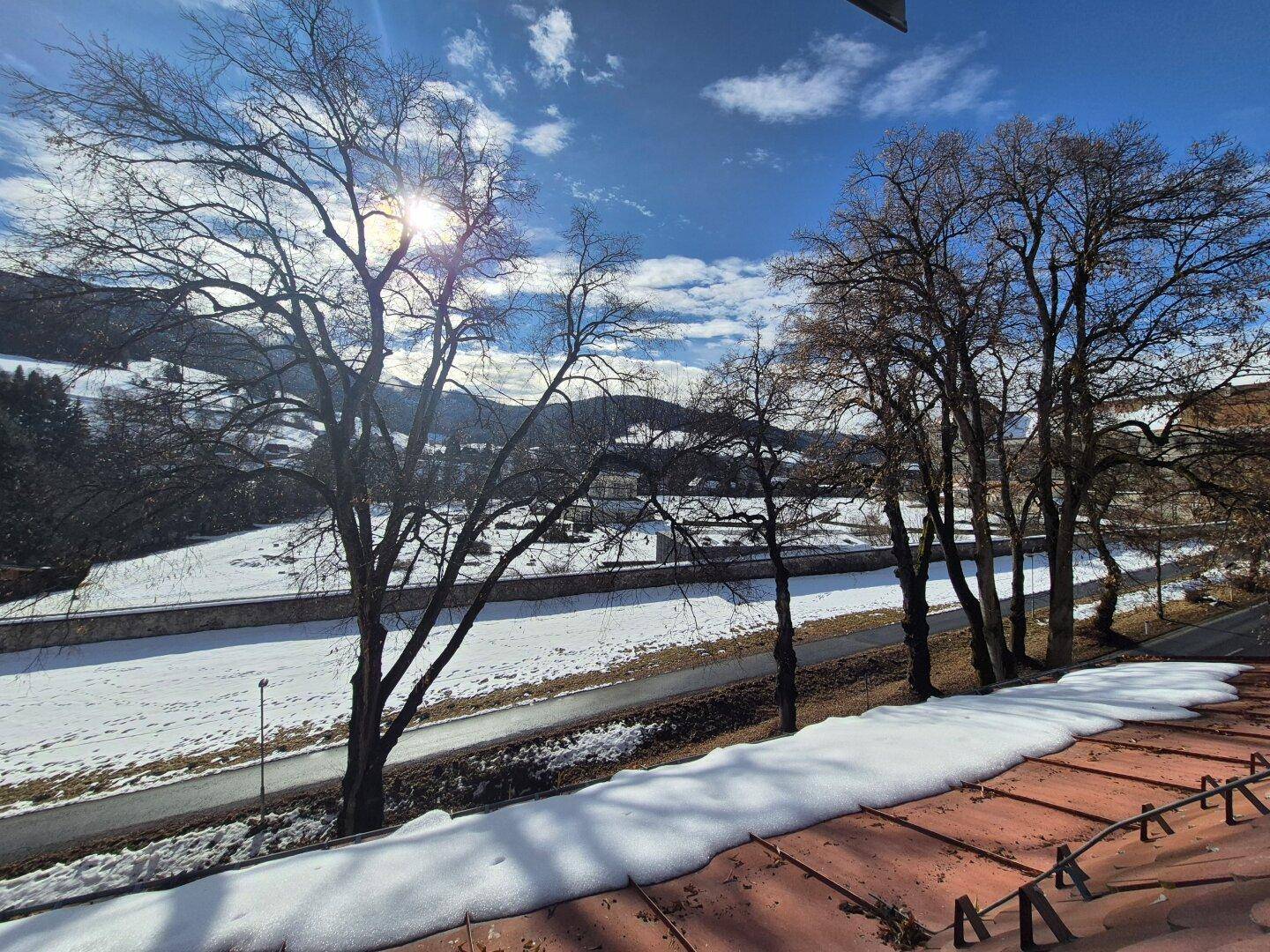 Weite Aussicht auf die verschneite Landschaft mit Bäumen und Bergen unter blauem Himmel.