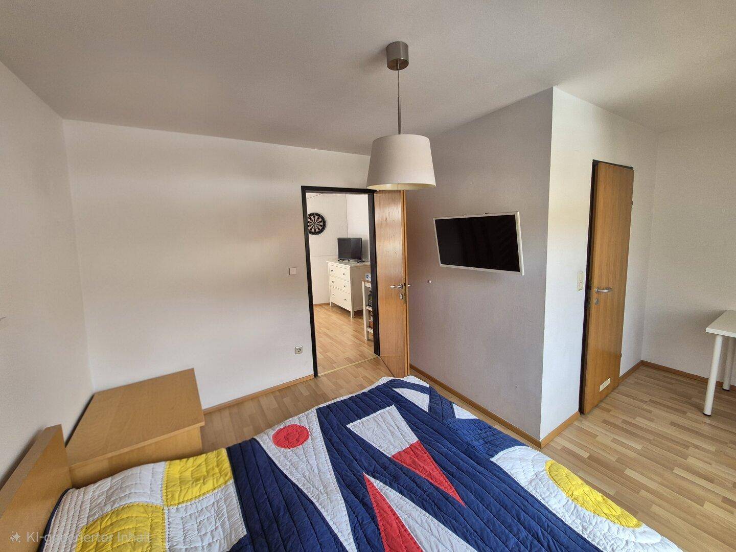 Schlafzimmer mit Holzboden, Bett und Zugang zu einem anderen Raum.