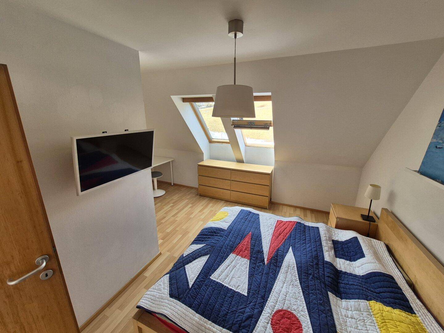 Schlafzimmer mit Holzboden, Wand-TV und Dachfenstern, die viel Licht spenden.