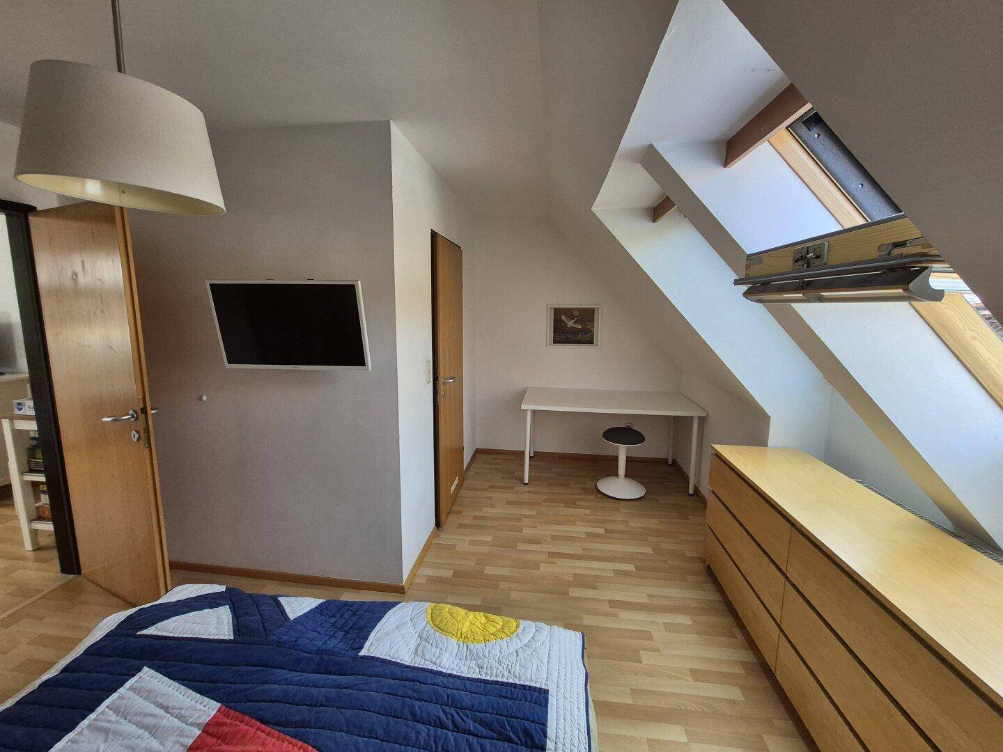 Schlafzimmer mit Holzboden, Schreibtisch und Dachschräge, ideal für Home-Office.