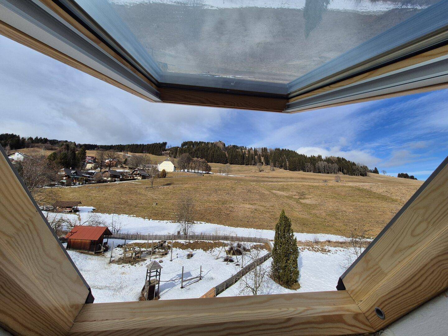 Weite Aussicht auf die ländliche Umgebung mit Hügeln und Schnee von einem Dachfenster.
