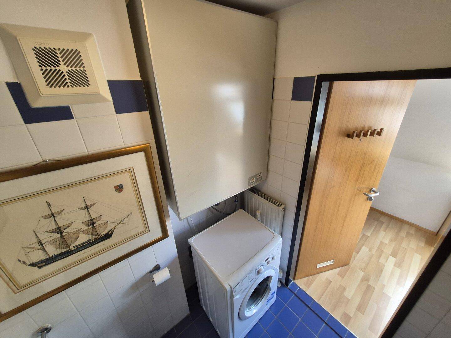 Badezimmer mit Waschmaschine, Lüftung und blauen Fliesen, funktional und sauber.