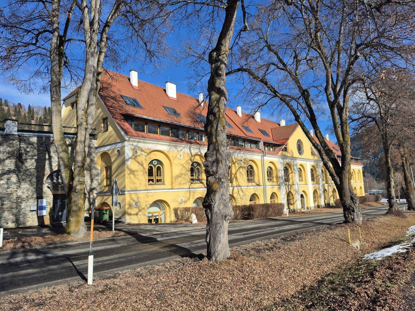 Historisches Gebäude mit markanter gelber Fassade und vielen Fenstern in ländlicher Umgebung.