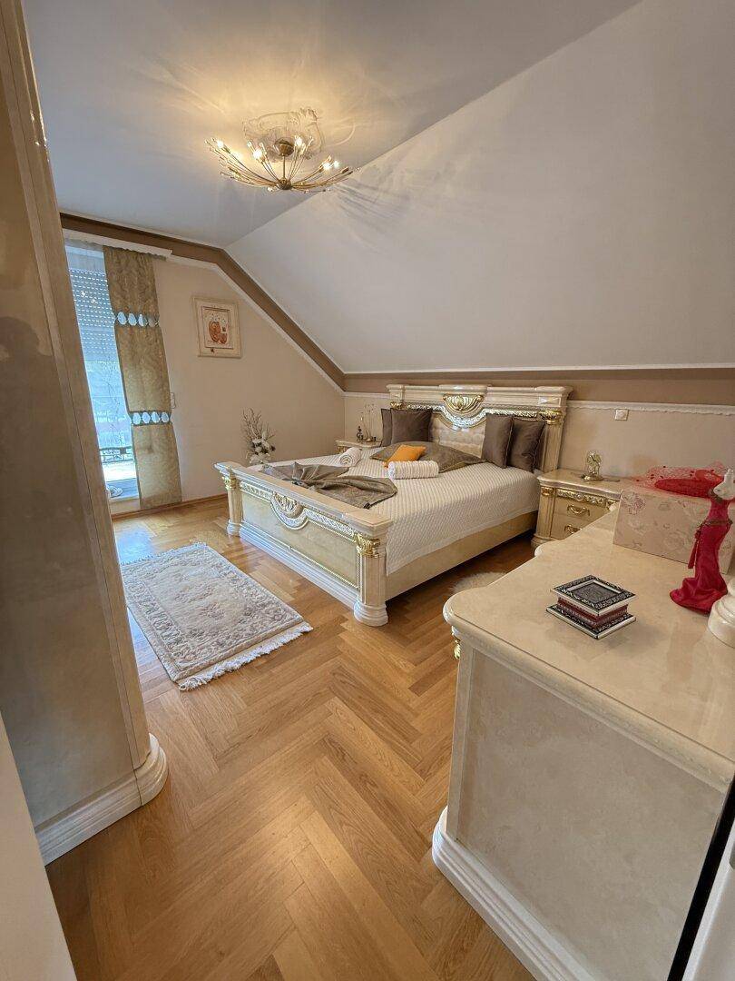 Elegantes Schlafzimmer mit Parkettboden, luxuriösem Bett und Dachschräge.