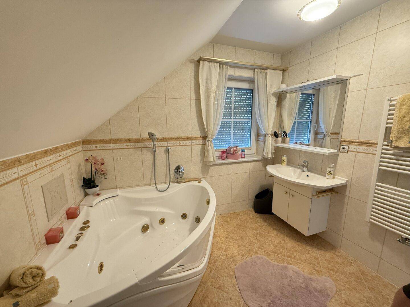 Badezimmer mit Eck-Whirlpool, Fliesen und Fenster unter der Dachschräge.