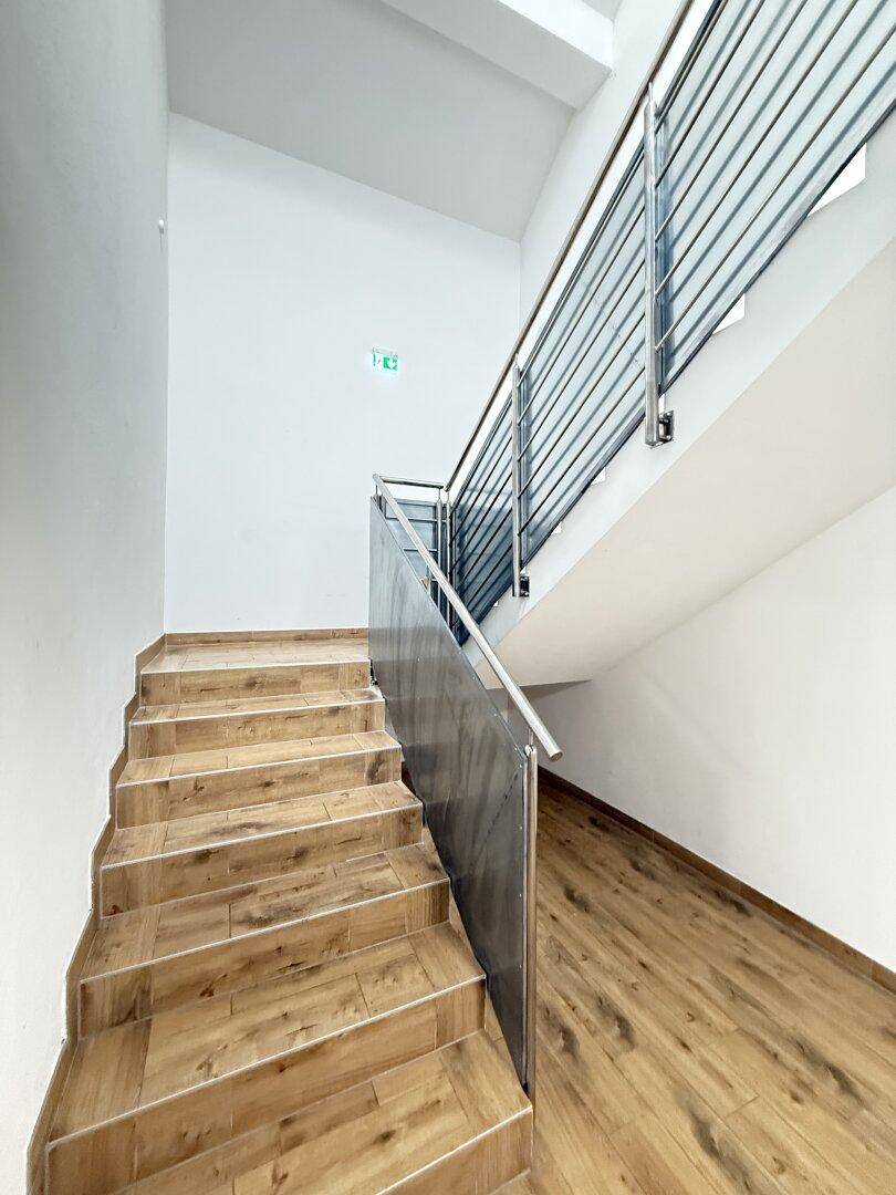 Modernes Treppenhaus mit Holzoptik-Stufen und Edelstahlgeländer.