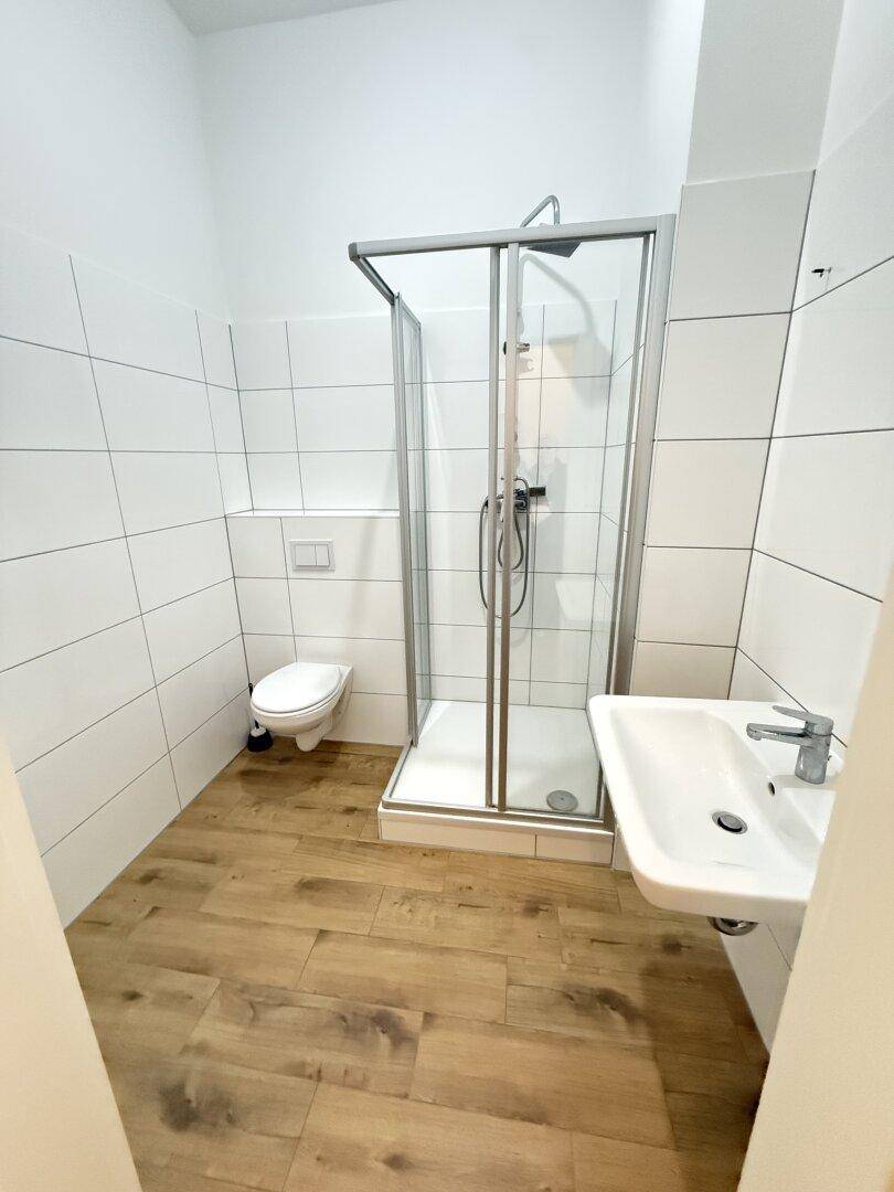 Modernes Badezimmer mit weiß gefliesten Wänden, Dusche und Waschbecken.