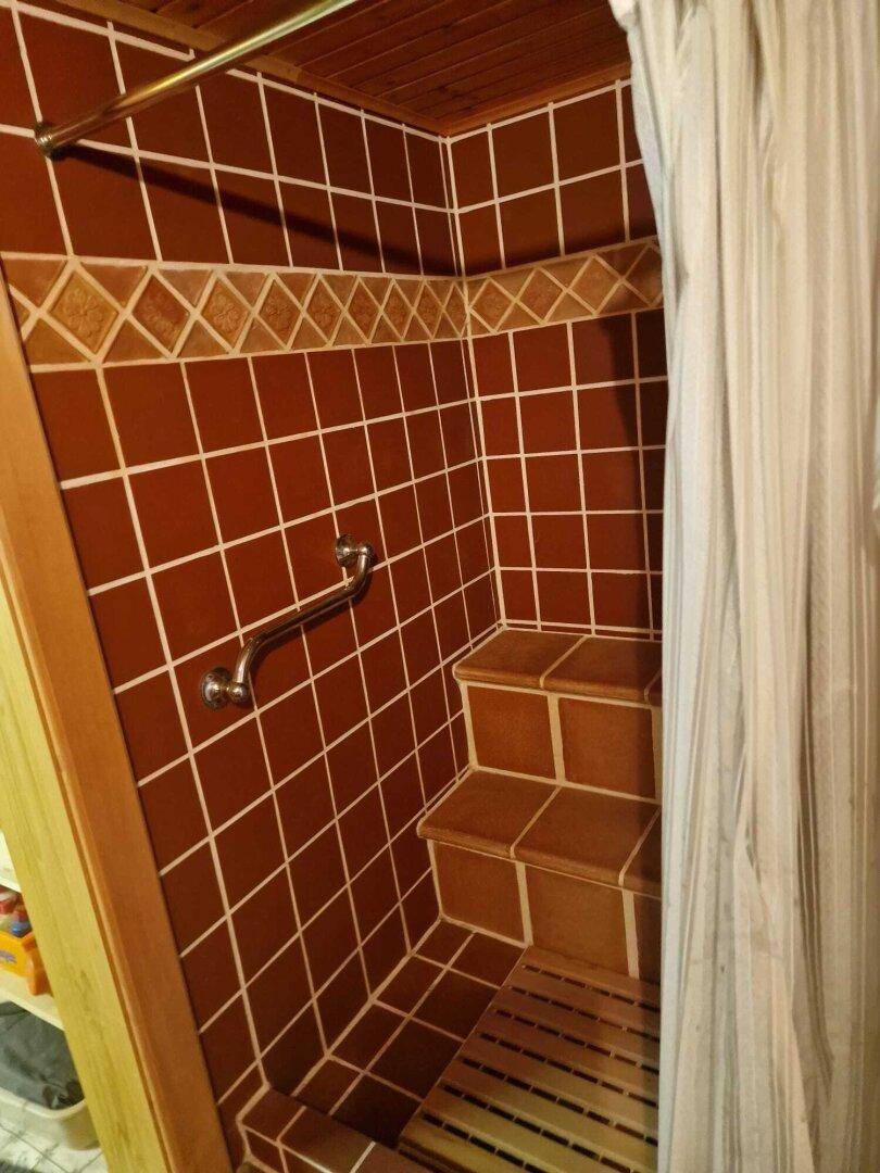 Geflieste Dusche mit Haltegriff und Holzrost, im traditionellen Stil, sicher und funktional.
