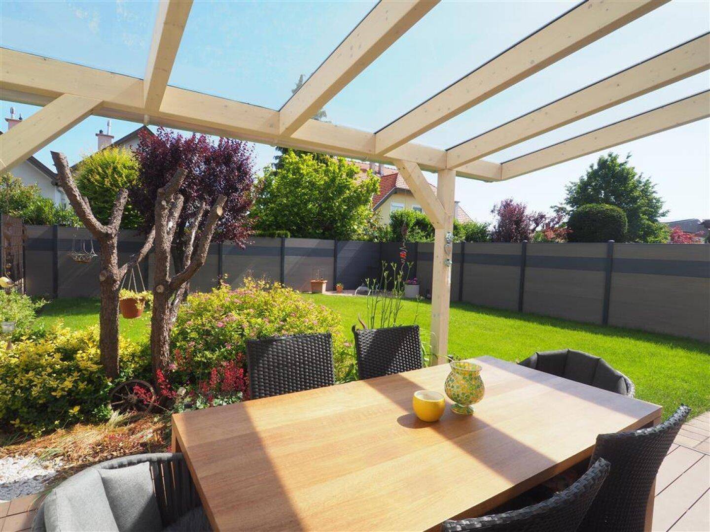 Gemütlicher Essbereich auf der überdachten Terrasse mit Holztisch und Blick in den grünen Garten.