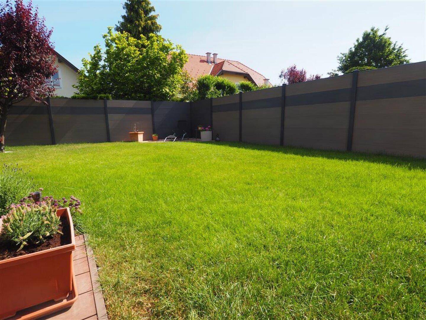 Großer, gepflegter Rasenbereich im Garten, umgeben von einem modernen Sichtschutzzaun und Bäumen.