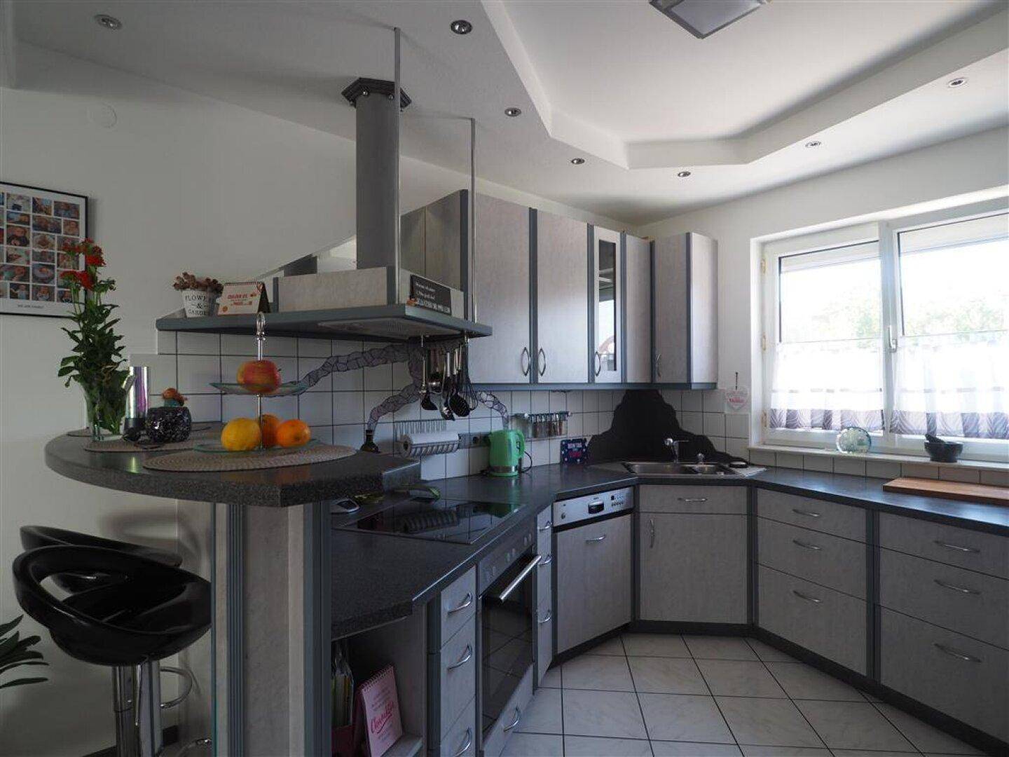 Moderne Küche mit grauen Fronten, integrierten Geräten und einem praktischen Frühstücksbereich am Fenster.