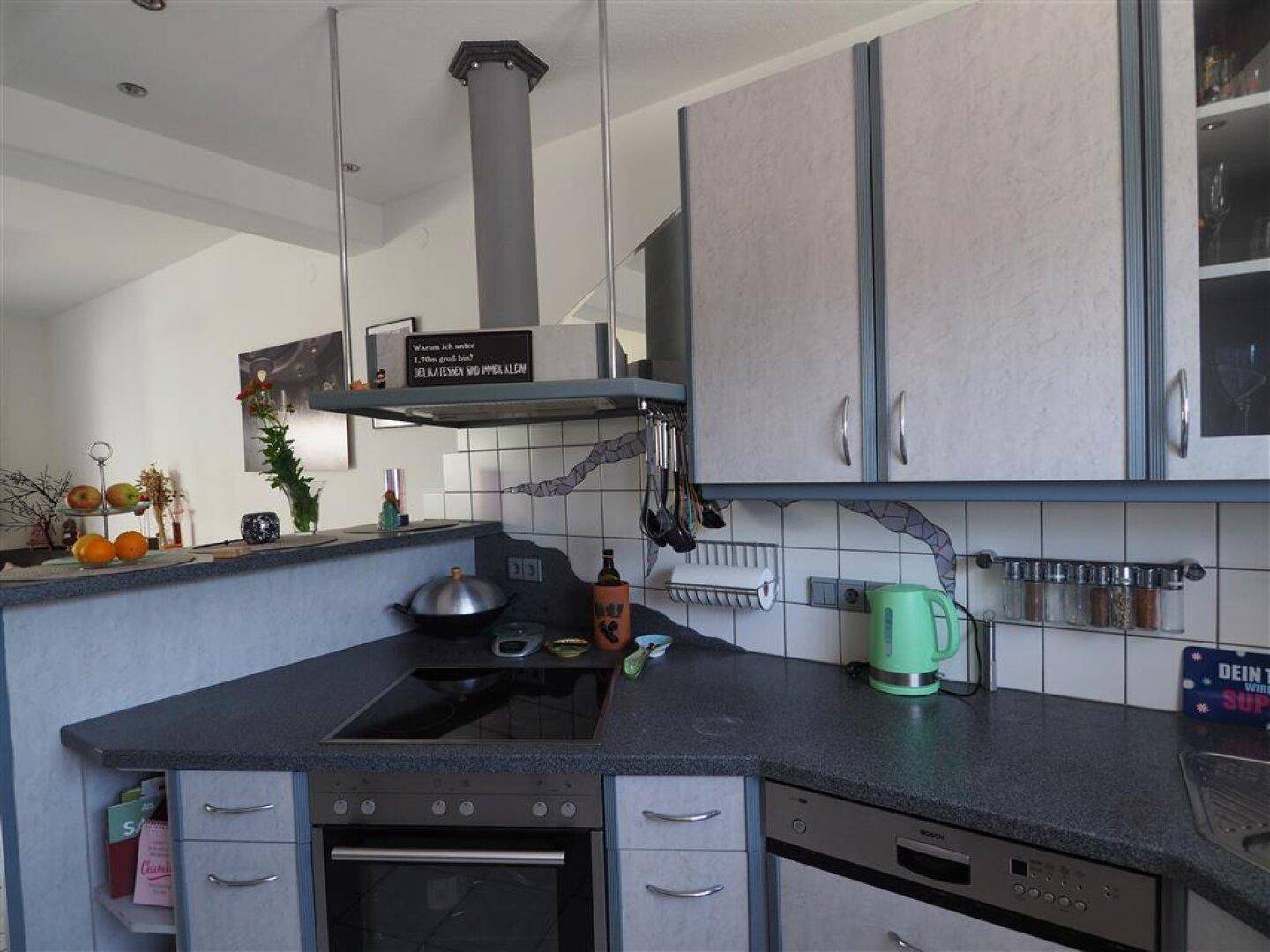 Detailansicht der modernen Küche mit Kochfeld, Dunstabzugshaube und Fliesenrückwand in Grau.