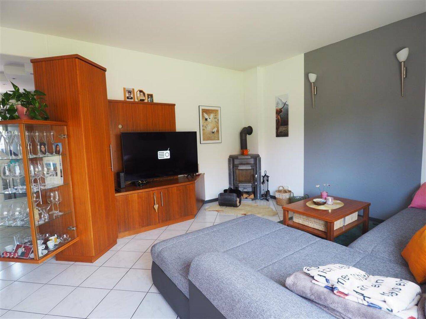 Geräumiges Wohnzimmer mit Kaminofen, bequemer Sitzecke und Holzmöbeln für eine warme Atmosphäre.