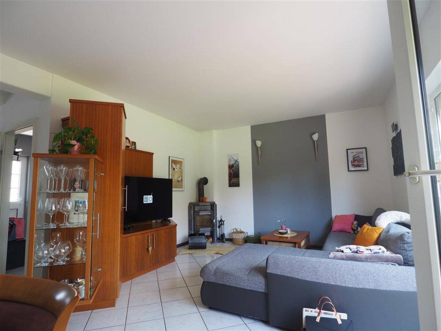 Helles Wohnzimmer mit Kaminofen, großem Sofa und Blick auf den grünen Gartenbereich.