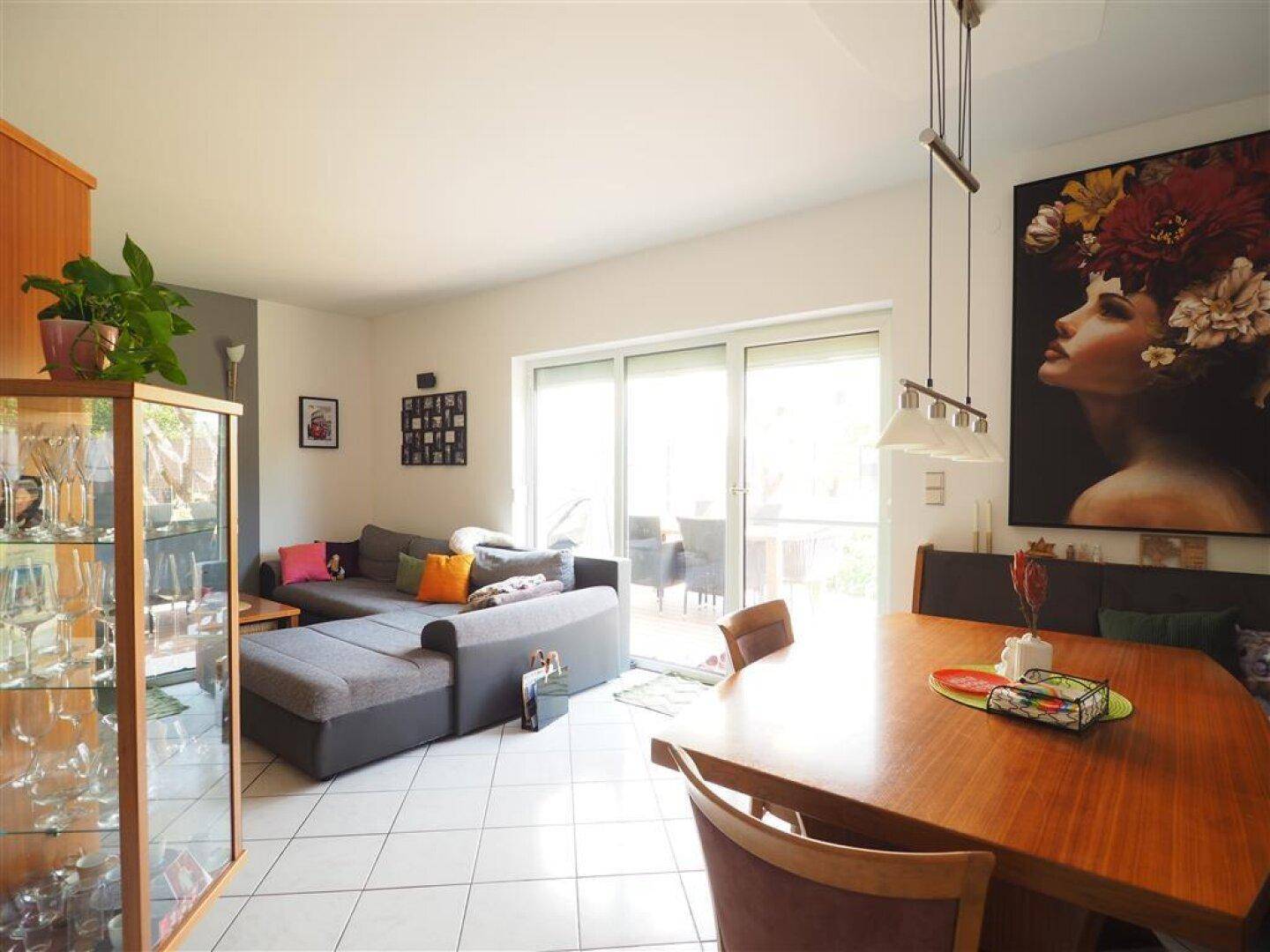 Heller Wohn- und Essbereich mit Fliesenboden, großem Sofa und direktem Zugang zur Terrasse.