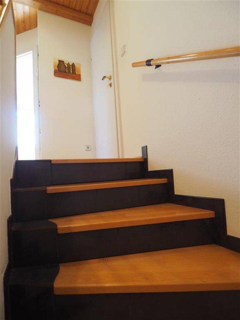 Holztreppe mit dunklen Stufen und hellem Handlauf, die in die obere Etage des Hauses führt.