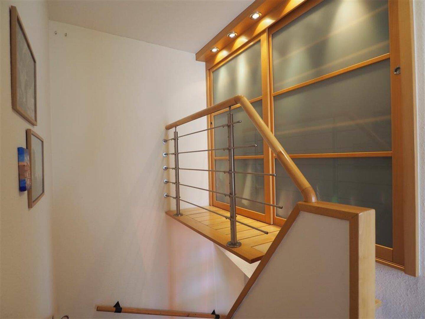 Moderne Holztreppe mit Edelstahlgeländer und integrierter Beleuchtung, die zum Obergeschoss führt.