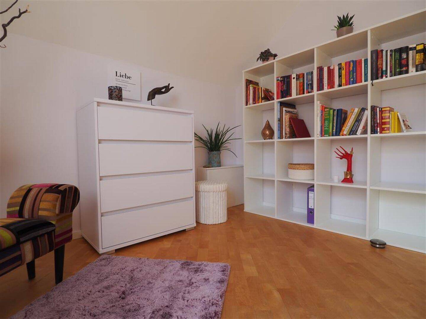 Geräumiges Arbeitszimmer mit viel Stauraum in Regalen und Kommoden, sowie Holzboden und Tageslicht.