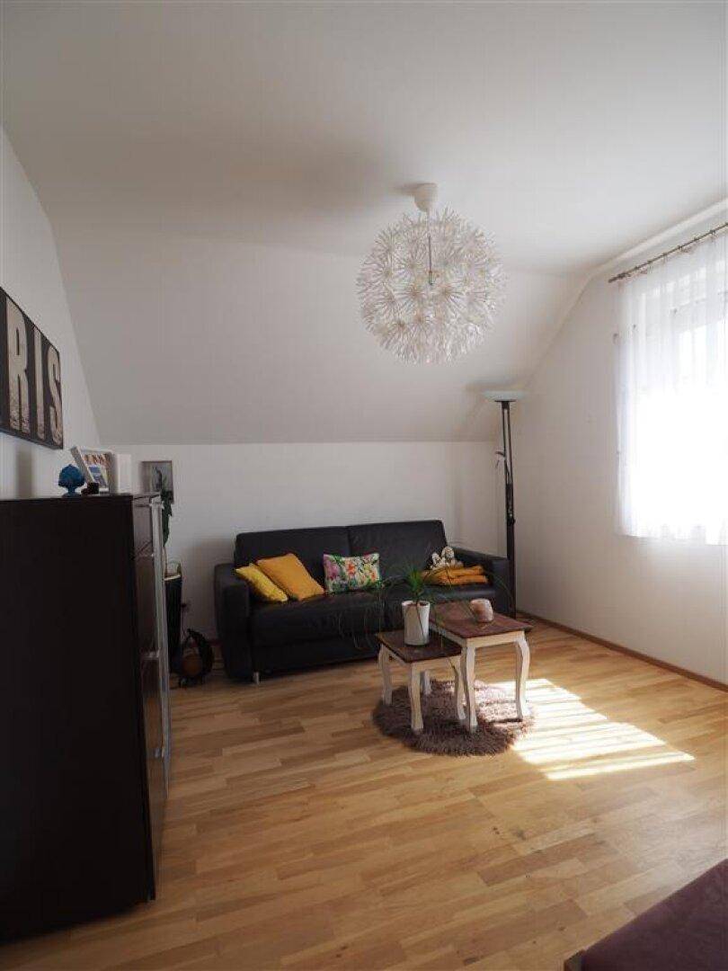 Helles Wohnzimmer mit viel Tageslicht, Sofa und Holzboden unter der Dachschräge.