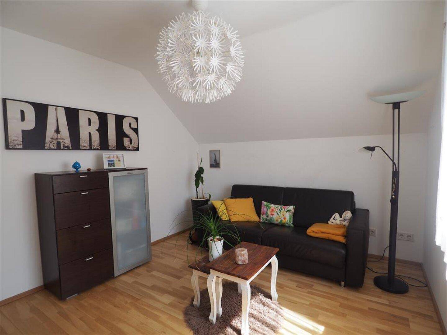 Gemütliches Wohnzimmer unter Dachschräge mit Sofa, Couchtisch und Holzboden für entspannte Stunden.