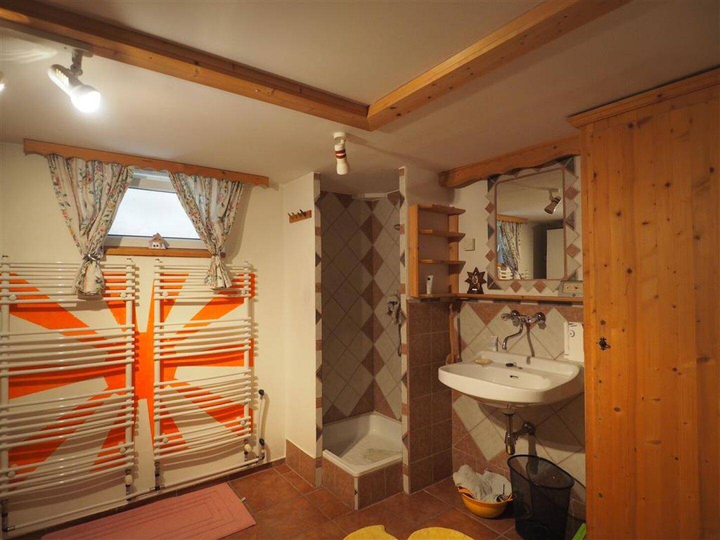 Kellerbadezimmer mit Dusche, Waschbecken und Spiegel, ausgestattet mit Fliesenboden und Holzdeckenbalken.