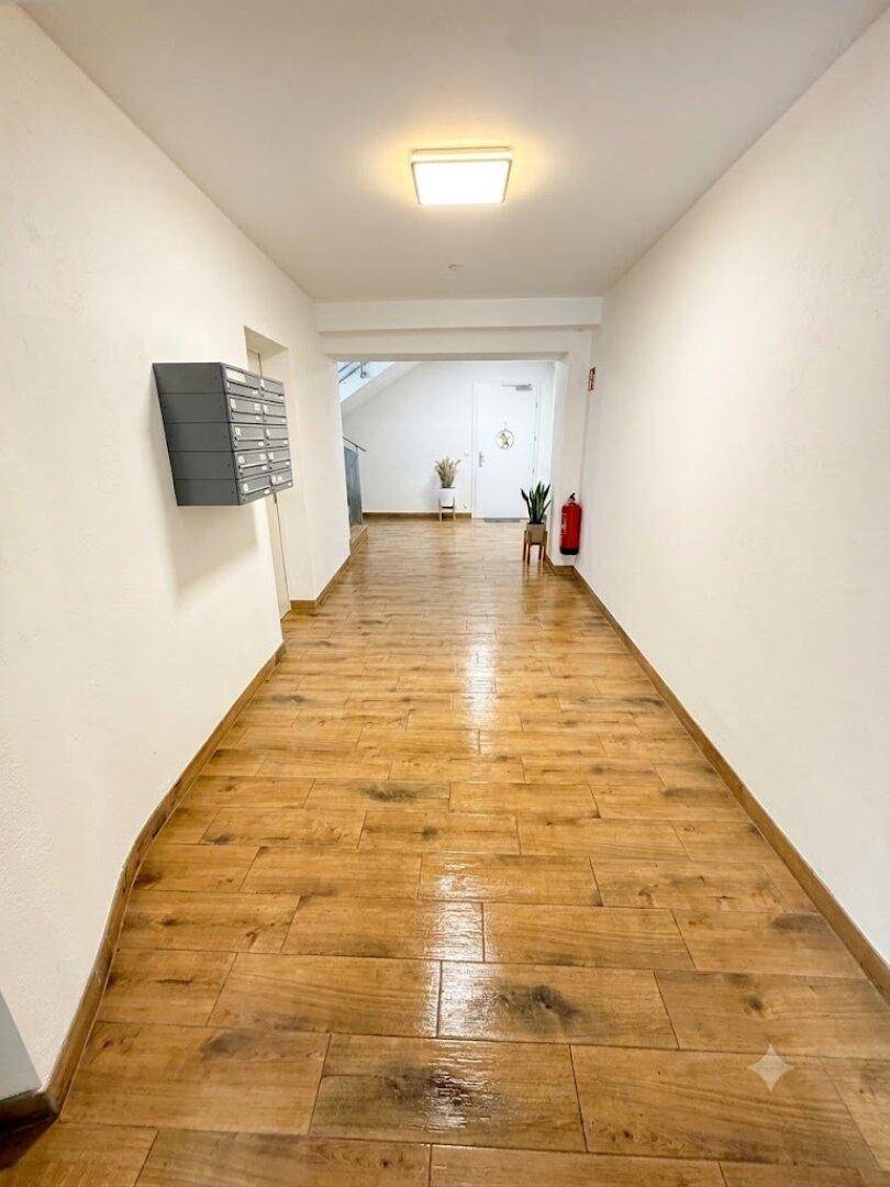 Heller Flur mit Holzoptik-Fliesenboden und Briefkästen an der Wand.
