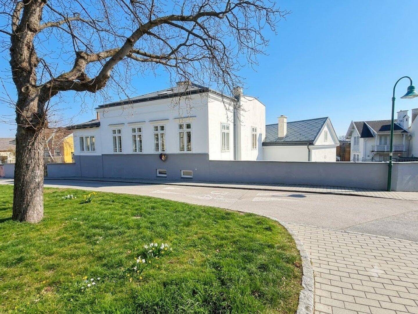 Historisches Gebäude mit weißer Fassade und grauer Sockelzone an einer Straße.