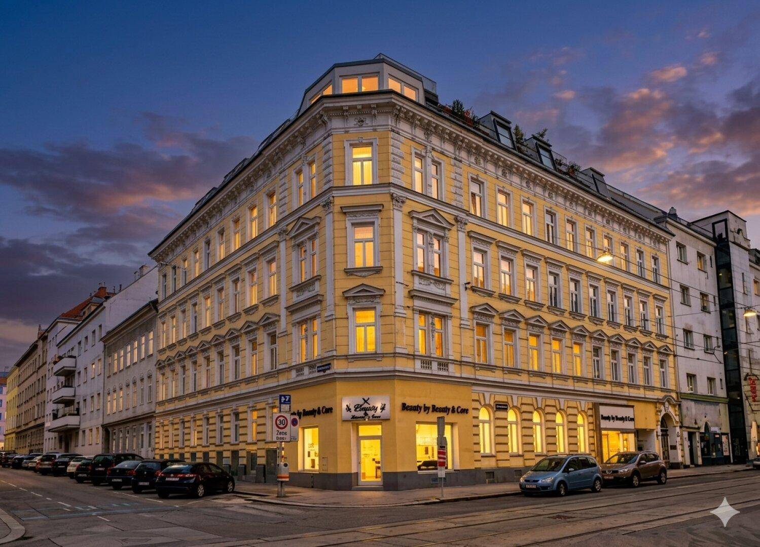 Historisches Eckgebäude bei Sonnenuntergang mit beleuchteten Fenstern und gelber Fassade.