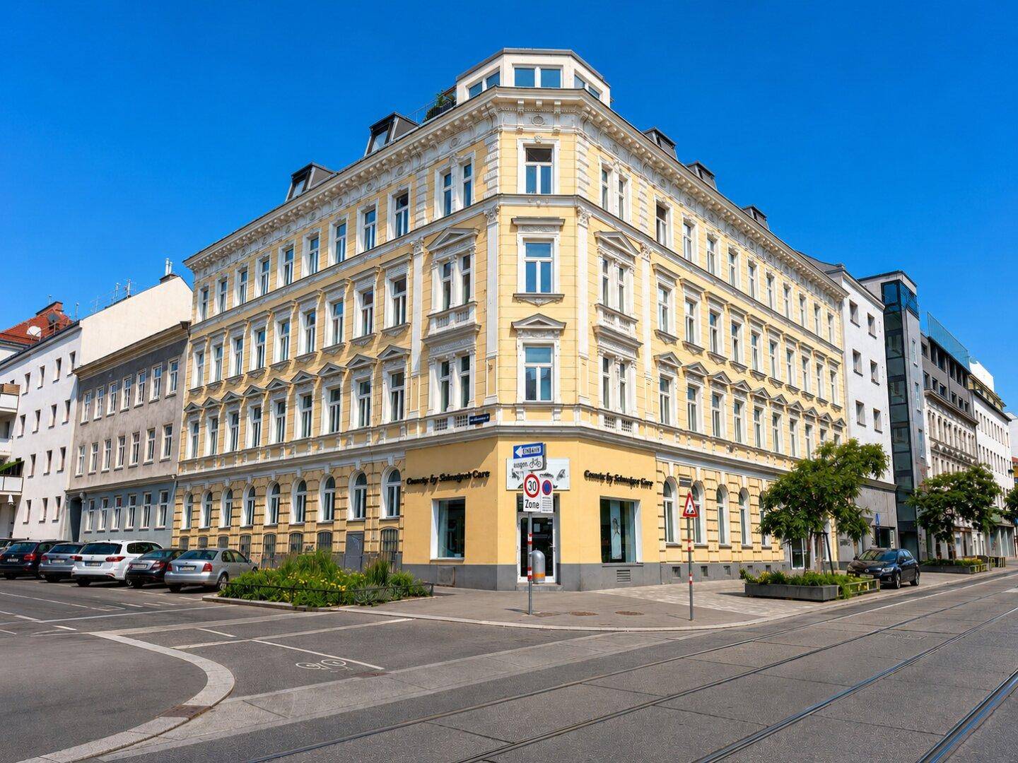 Historisches Eckgebäude mit gelber Fassade und vielen Fenstern an einer belebten Straße.