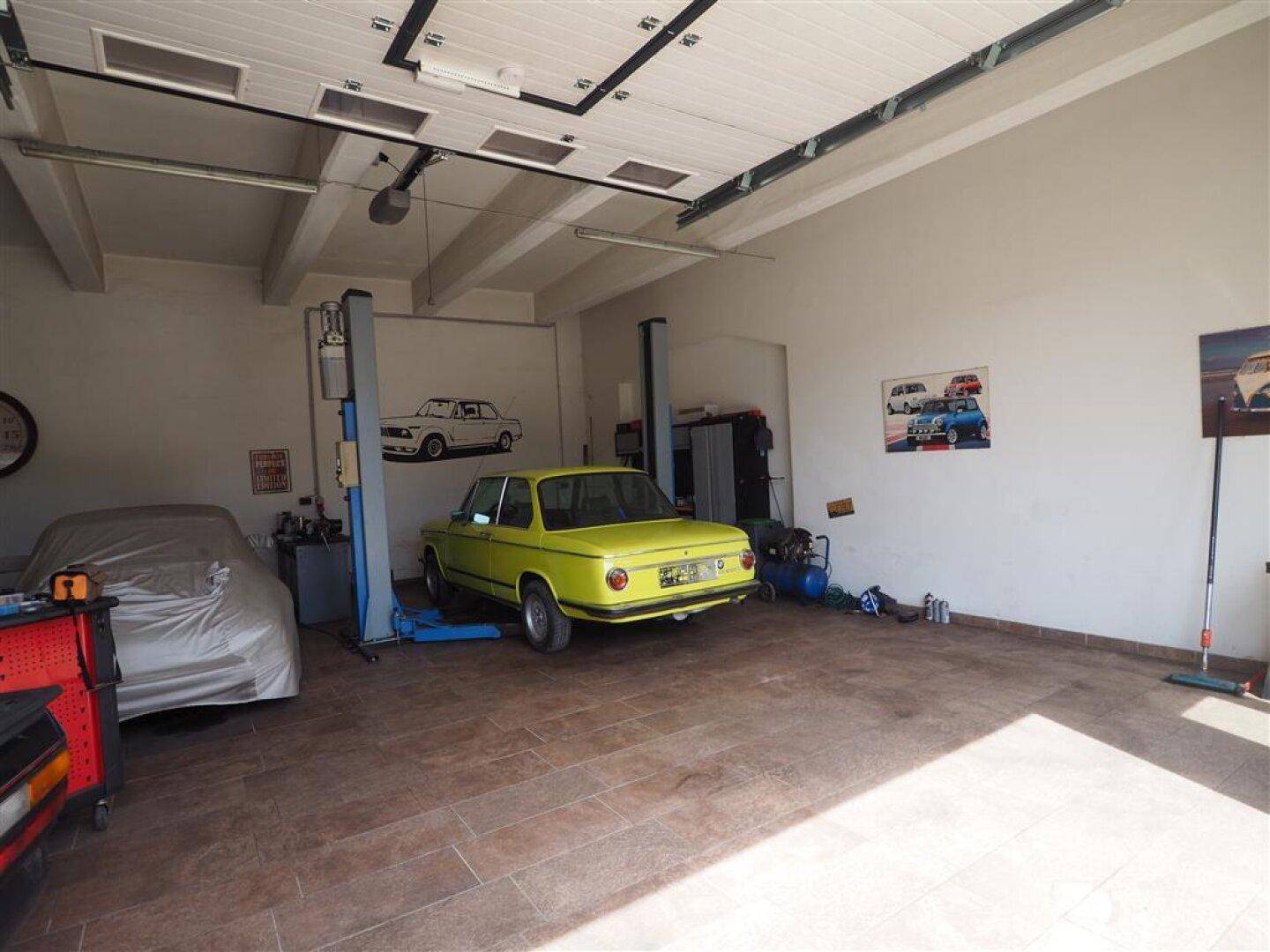 Geräumige Autowerkstatt mit mehreren Fahrzeugen, Hebebühnen und gefliestem Boden.