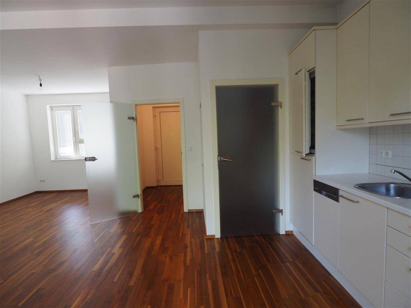 Geräumiger Wohnbereich mit dunklem Holzboden und modernen Glastüren zu angrenzenden Räumen.