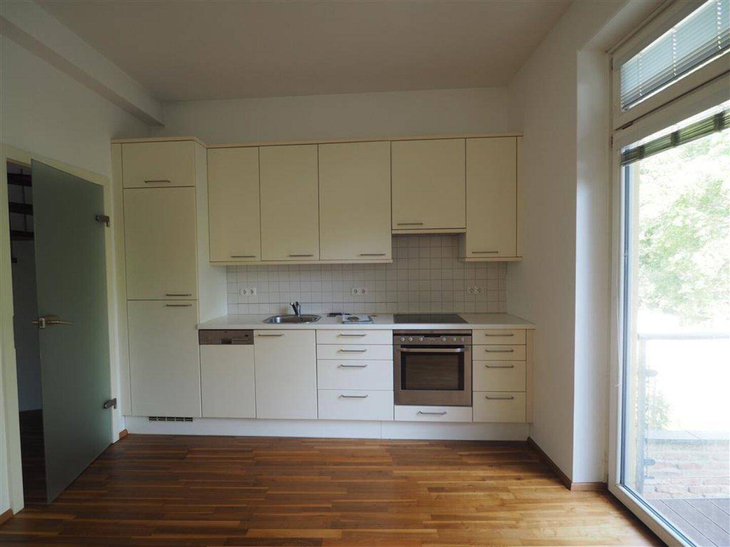 Funktionale Küche mit beigefarbenen Schränken, Holzboden und Zugang zu einem Balkon.
