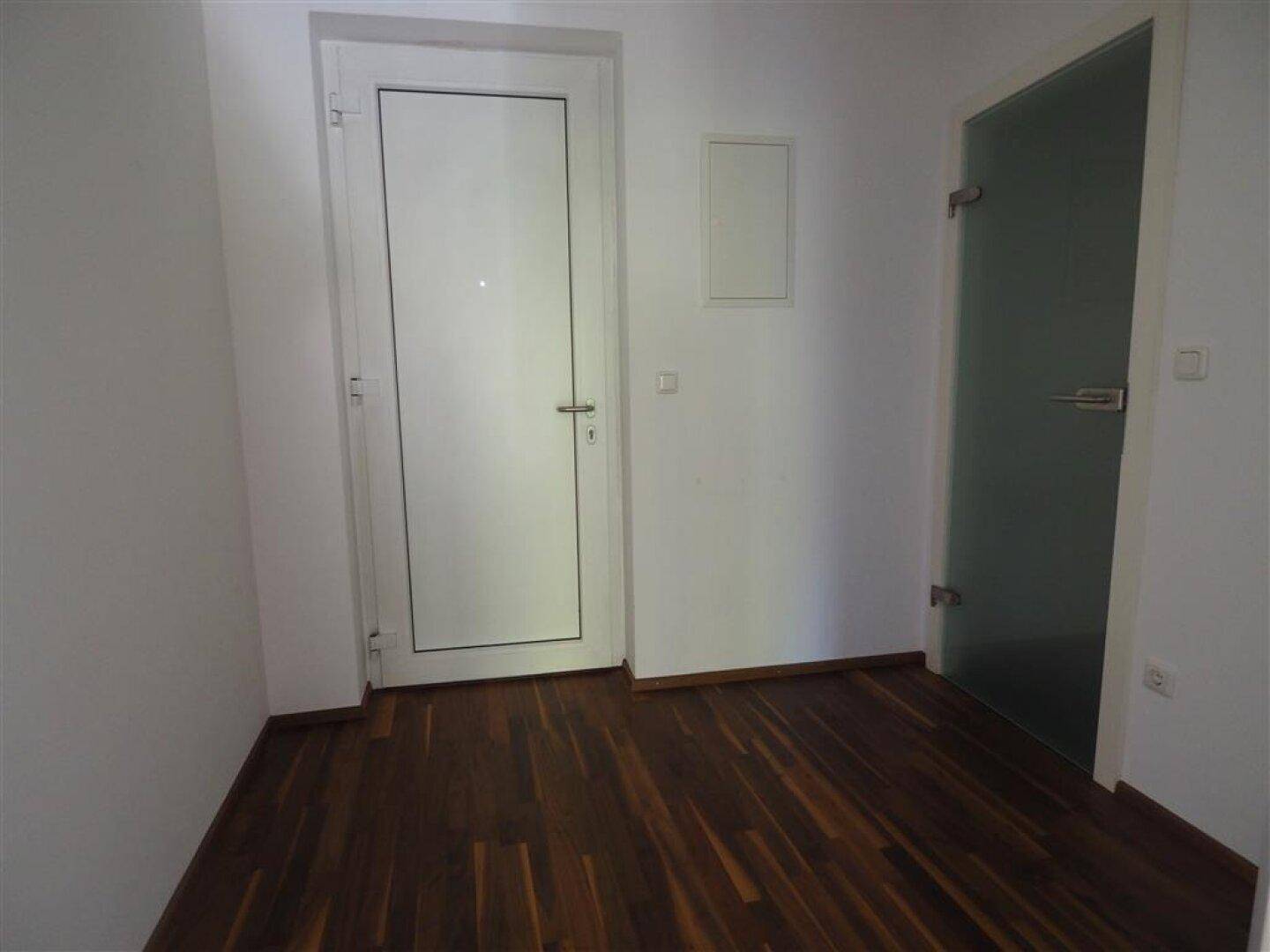 Heller Flur mit Holzboden, weißer Tür und einer modernen Milchglastür.