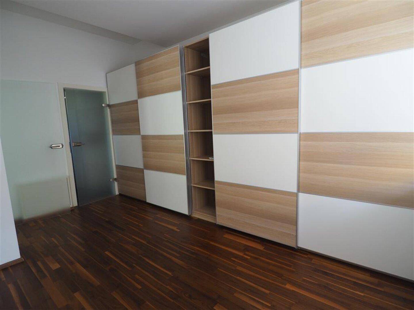 Schlafzimmer mit Holzboden und einem großen, modernen Einbauschrank mit Schiebetüren.