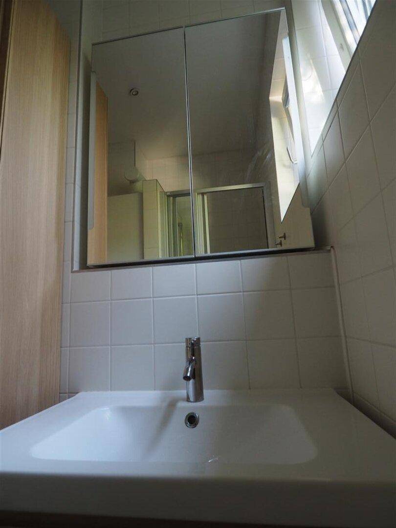 Helles Badezimmer mit Waschbecken, Spiegelschrank und weißen Fliesen.