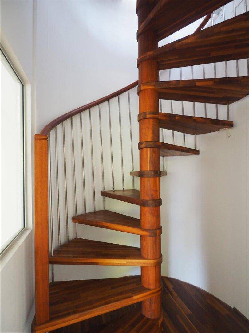 Elegante Holzwendeltreppe mit Metallgeländer, die verschiedene Ebenen des Hauses verbindet.