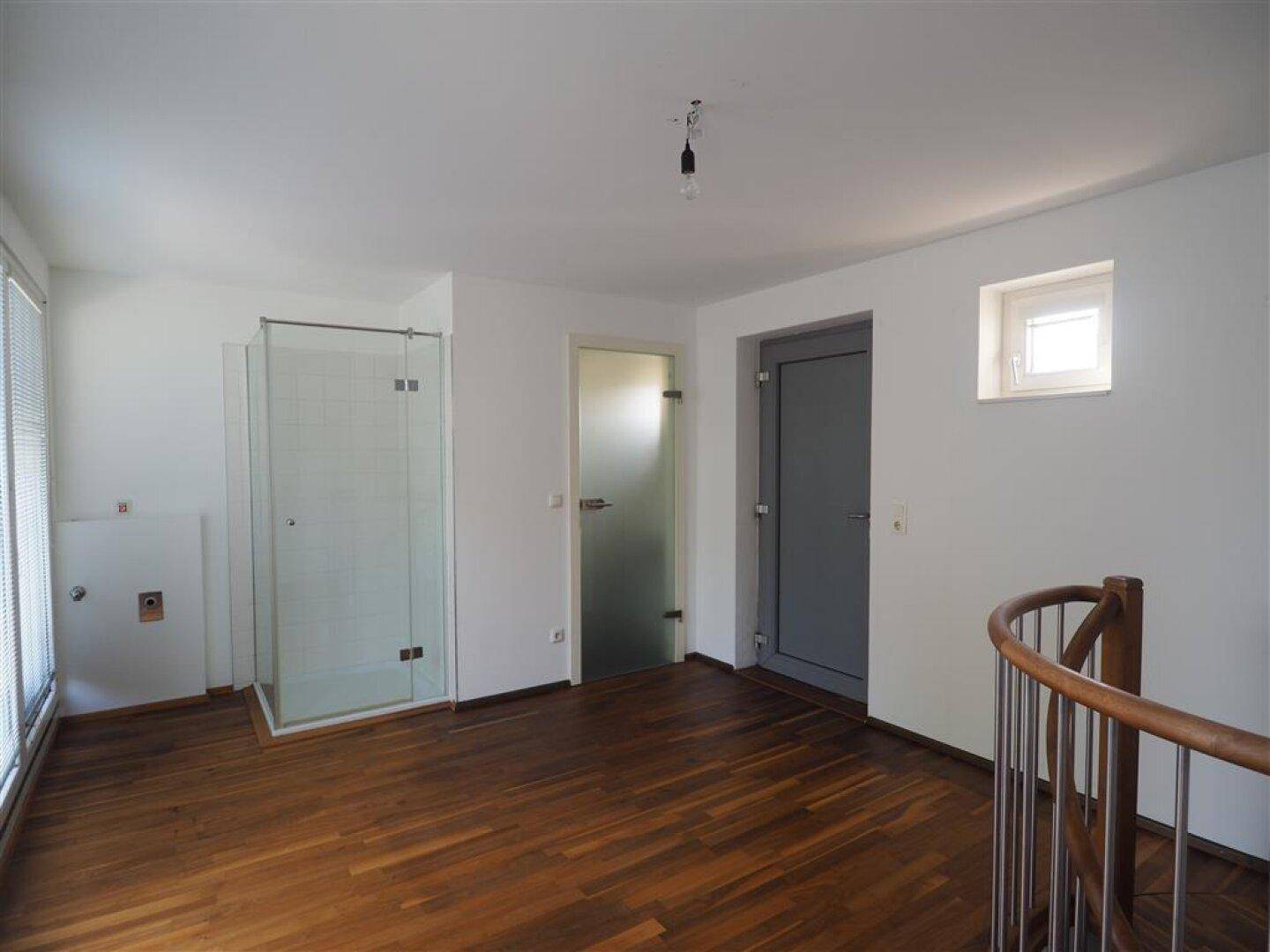 Offener Bereich im Obergeschoss mit Holzboden, Duschkabine und Wendeltreppe.