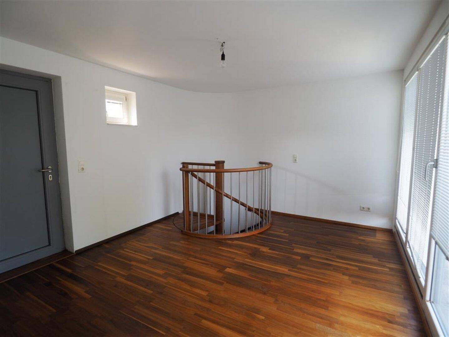 Heller offener Bereich mit Holzboden, Wendeltreppe und großen Fenstern.