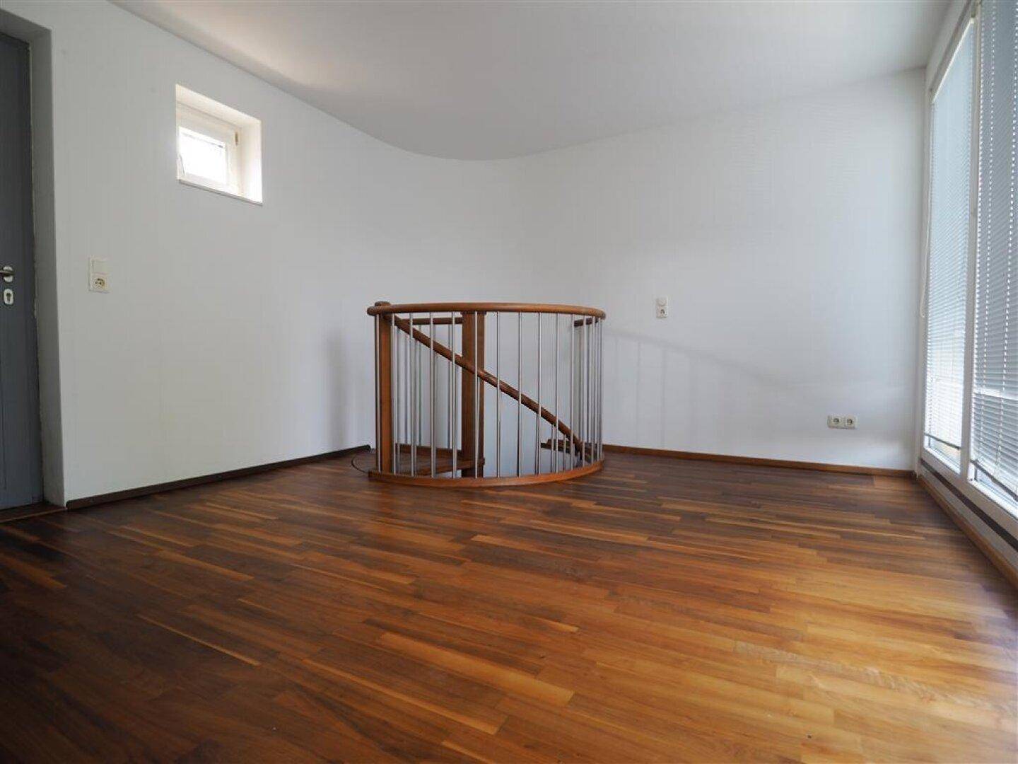 Geräumiger offener Bereich mit Holzboden und einer eleganten Wendeltreppe.