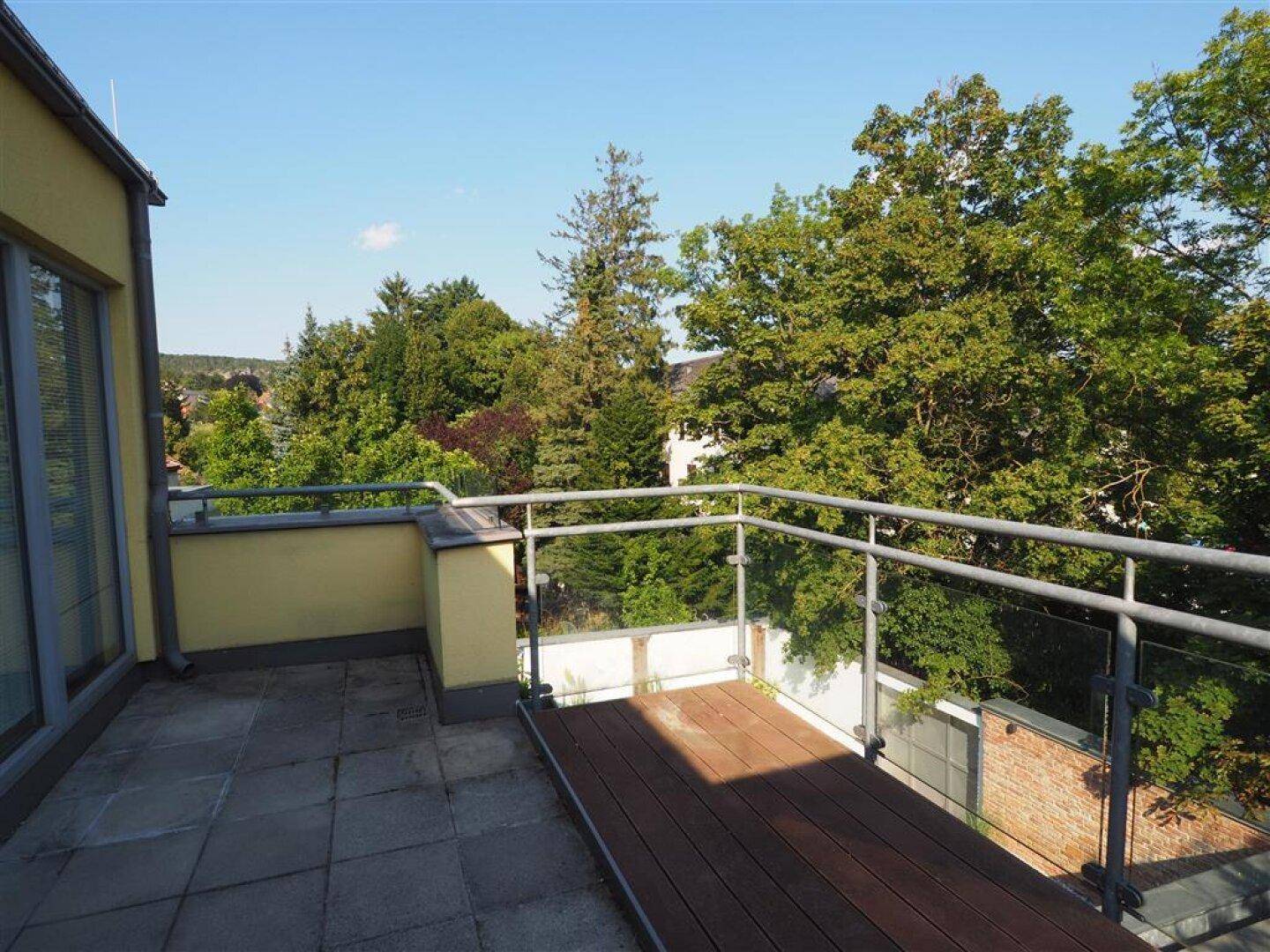 Große Dachterrasse mit Steinplatten und Holzdeck, umgeben von Bäumen und Weitblick.