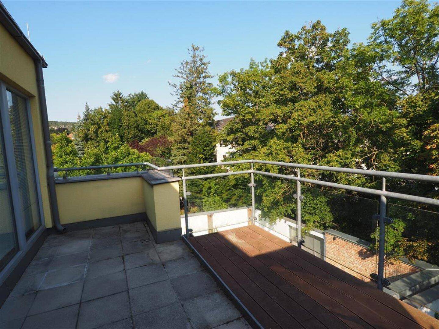 Geräumige Dachterrasse mit Steinplatten und Holzdeck, umgeben von viel Grün.