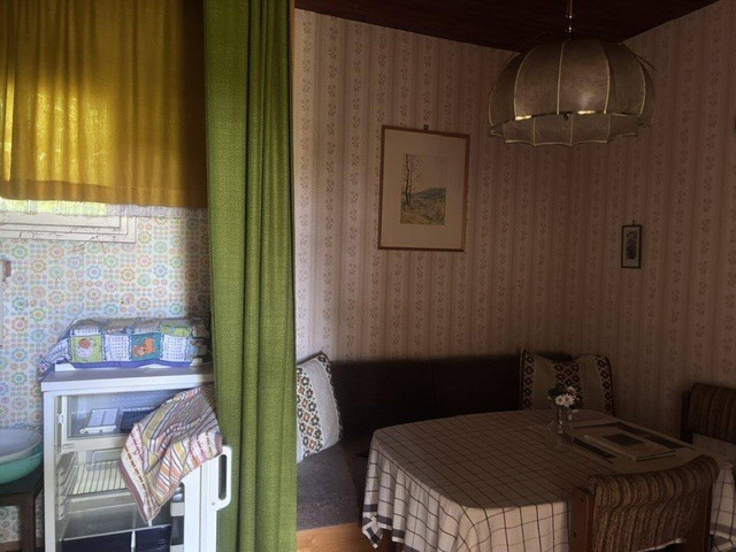 Essbereich mit gemusterter Tapete, rustikalen Möbeln und einem kleinen Kühlschrank neben dem Fenster.