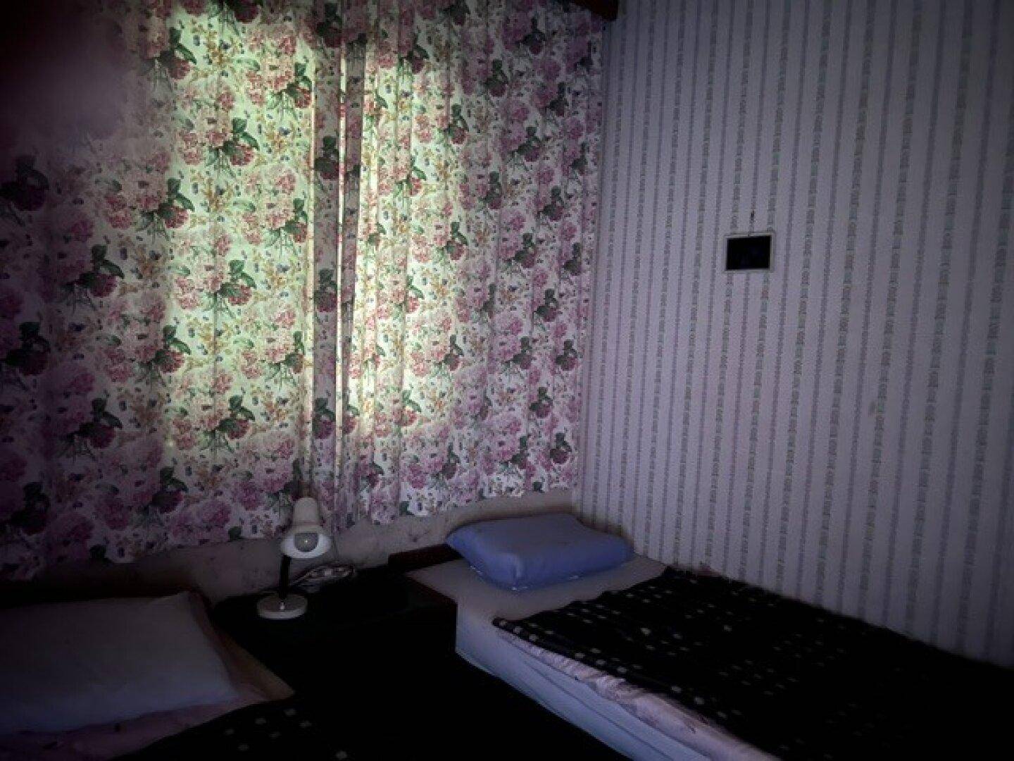 Schlafzimmer mit zwei Einzelbetten, floralen Vorhängen und gemusterter Tapete in gedämpftem Licht.